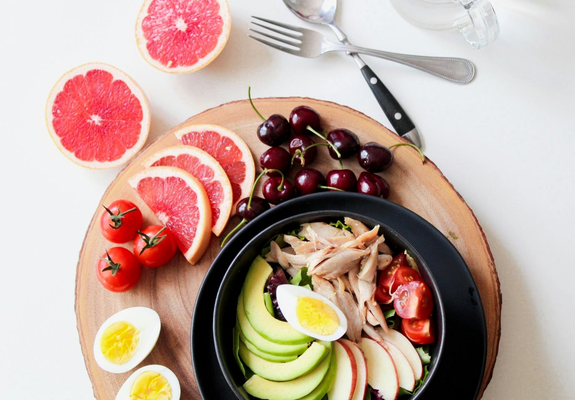 pexels photo 936611 936611 A vibrant breakfast flat lay featuring a mix of fruits, avocado, eggs, tomatoes, and sliced meats on a wooden platter.